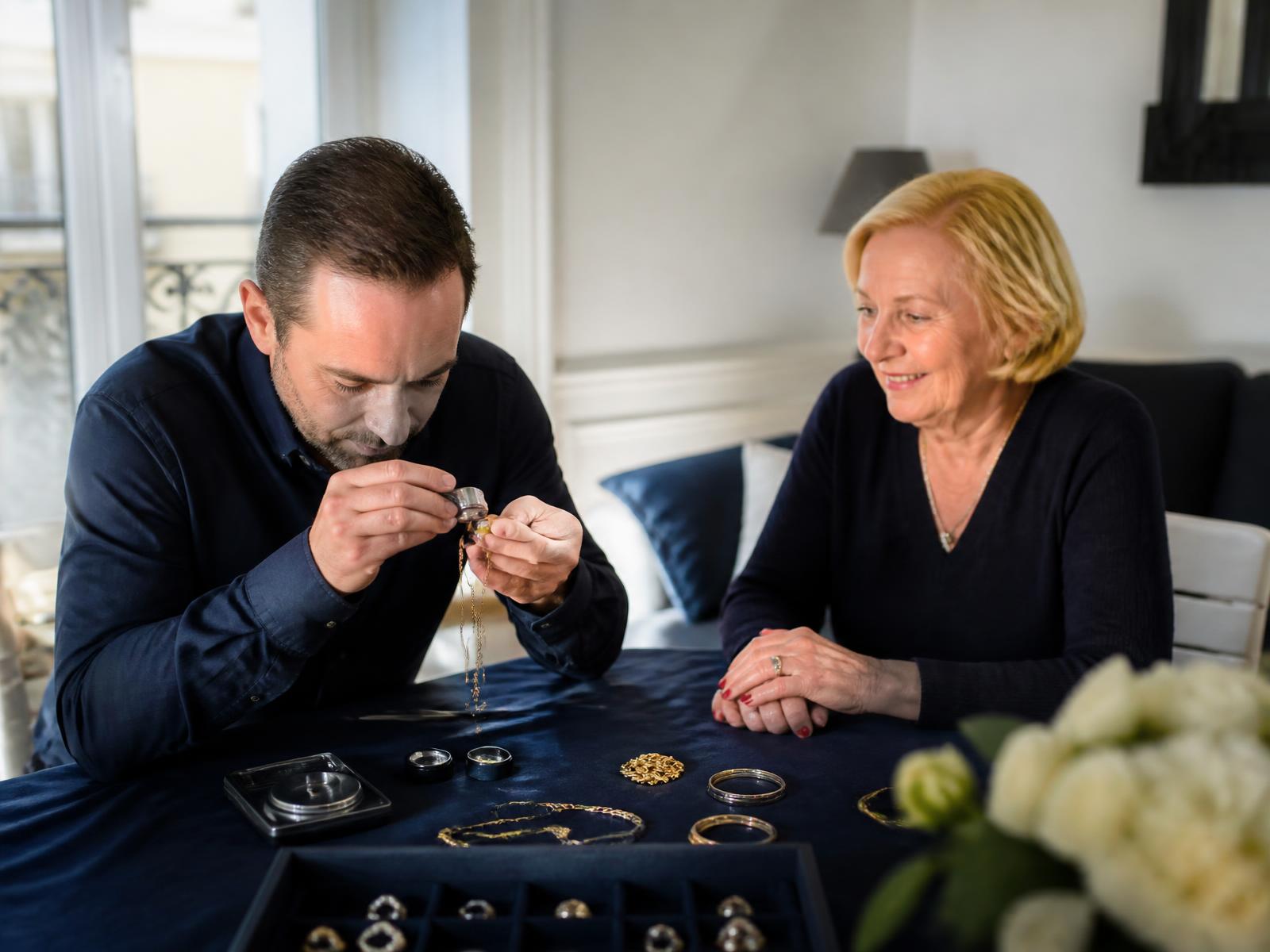 Expert en métaux précieux examinant des bijoux en or à la loupe, chez une particulière, à Lyon